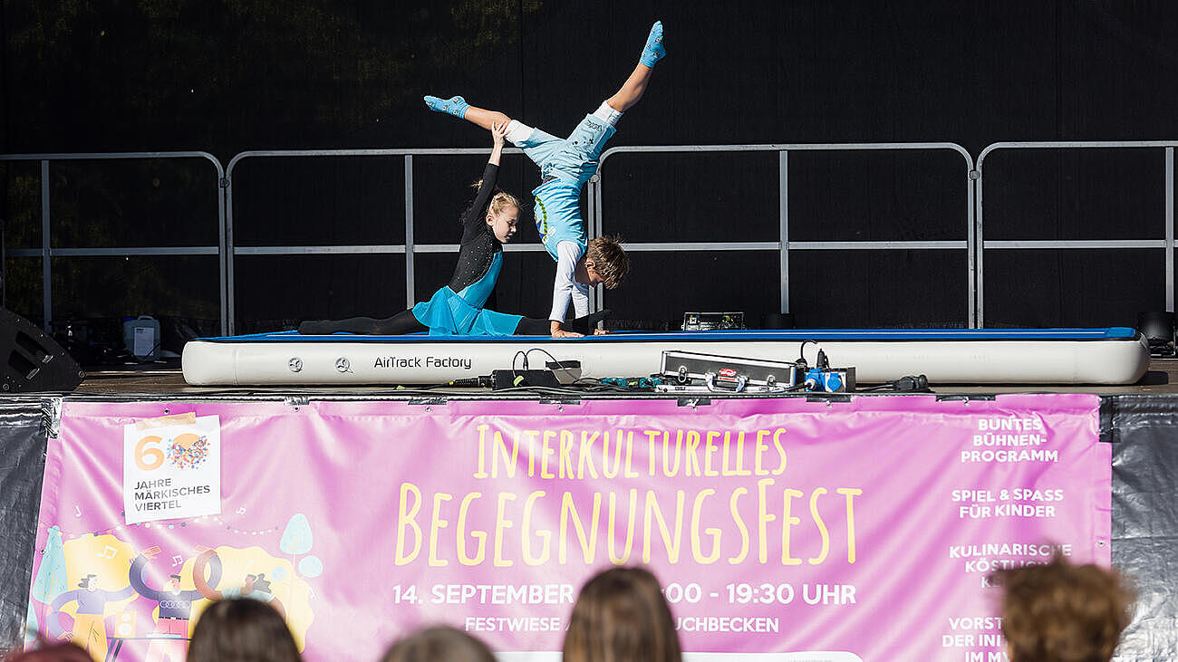 Zwei Kinder führen eine akrobatische Turnübung auf einer MAtratze auf der Bühne des Begegnungsfestes vor.