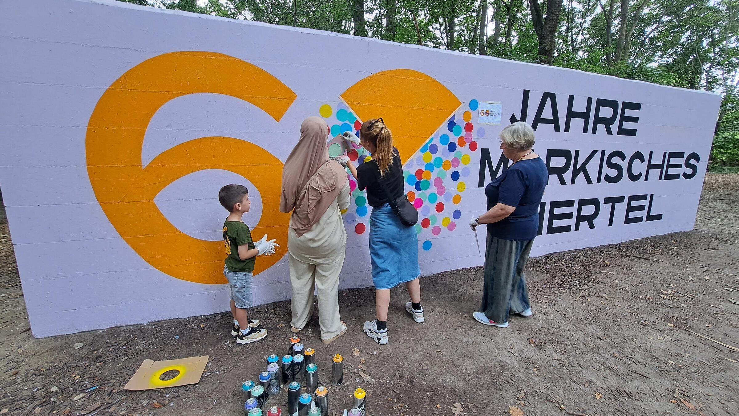 Außenaufnahme zeigt vier Personen, darunter ein Kind, beim Besprühen der Graffitiwand.