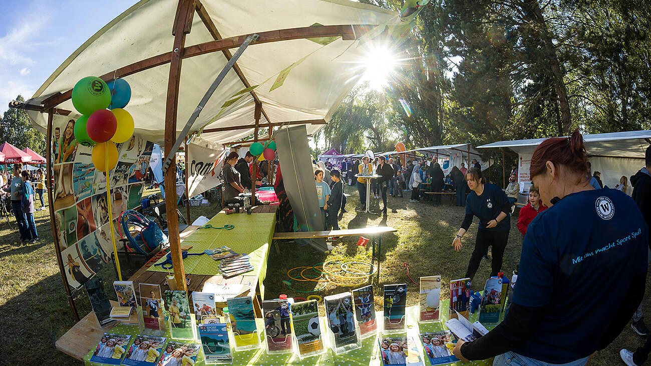 Weitwinkelaufnahme zeigt einen weiteren Stand auf dem Begegnungsfest mit Flyern und Aufstellern im Sonnenschein.