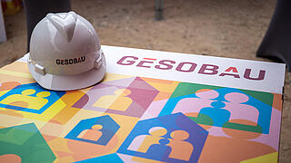 Bauhelm mit Logo "Gesobau" liegt auf einer bunten Unterlage
