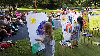 Außenaufnahme zeigt die Klax-Wiese mit jungen Künstler*innen vor ihren Leinwänden.