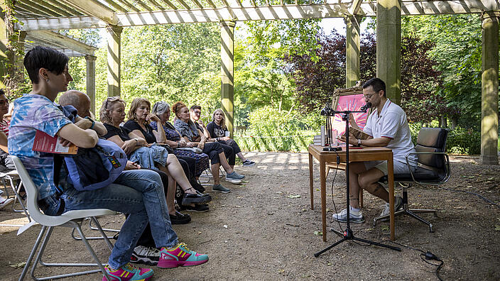 Kunstfest-Besucher hören in einer Pergola bei einer Autorenlesung zu.