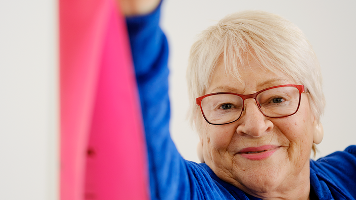 Innenaufnahme zeigt eine Seniorin beim Sport mit einem Dehnband.