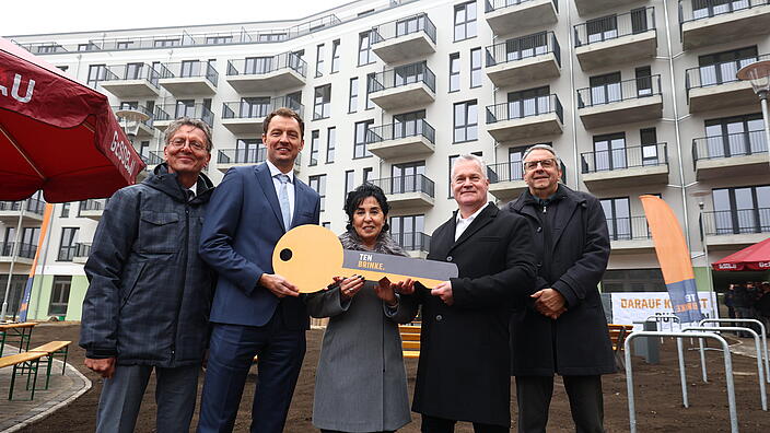 Bild zeigt Schlüsselübergabe in der Titiseestraße am 6. November 2024 (v.l.n.r.): Christian Gaebler (Senator Stadtentwicklung, Bauen und Wohnen), Arjen ten Brinke (Geschäftsführer Ten Brinke), Emine Demirbüken-Wegner (Bezirksbürgermeisterin Reinickendorf), Christian Wilkens (Vorstand GESOBAU) und Thomas Harms (Superintendent Kirchenkreis Reinickendorf). In der Mitte großer Schlüssel. Im Hintergrund Wohngebäude.