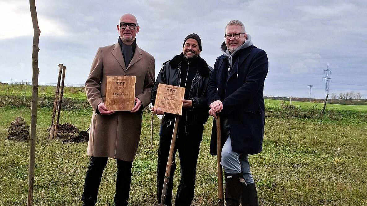 Bild zeigt  Jörg Franzen (Vorstandsvorsitzender GESOBAU AG), Jan Kinappel (Geschäftsführer Anschütz Entertainment Group Deutschland (AEG)), Jan Schierhorn (Initiator FAME FOREST) bei Kickoff für den FAME Forest Berlin. im Hintergrund Acker, im Vordergrund geplanzter Baum. Protagonisten halten Ehrentafel in der Hand.