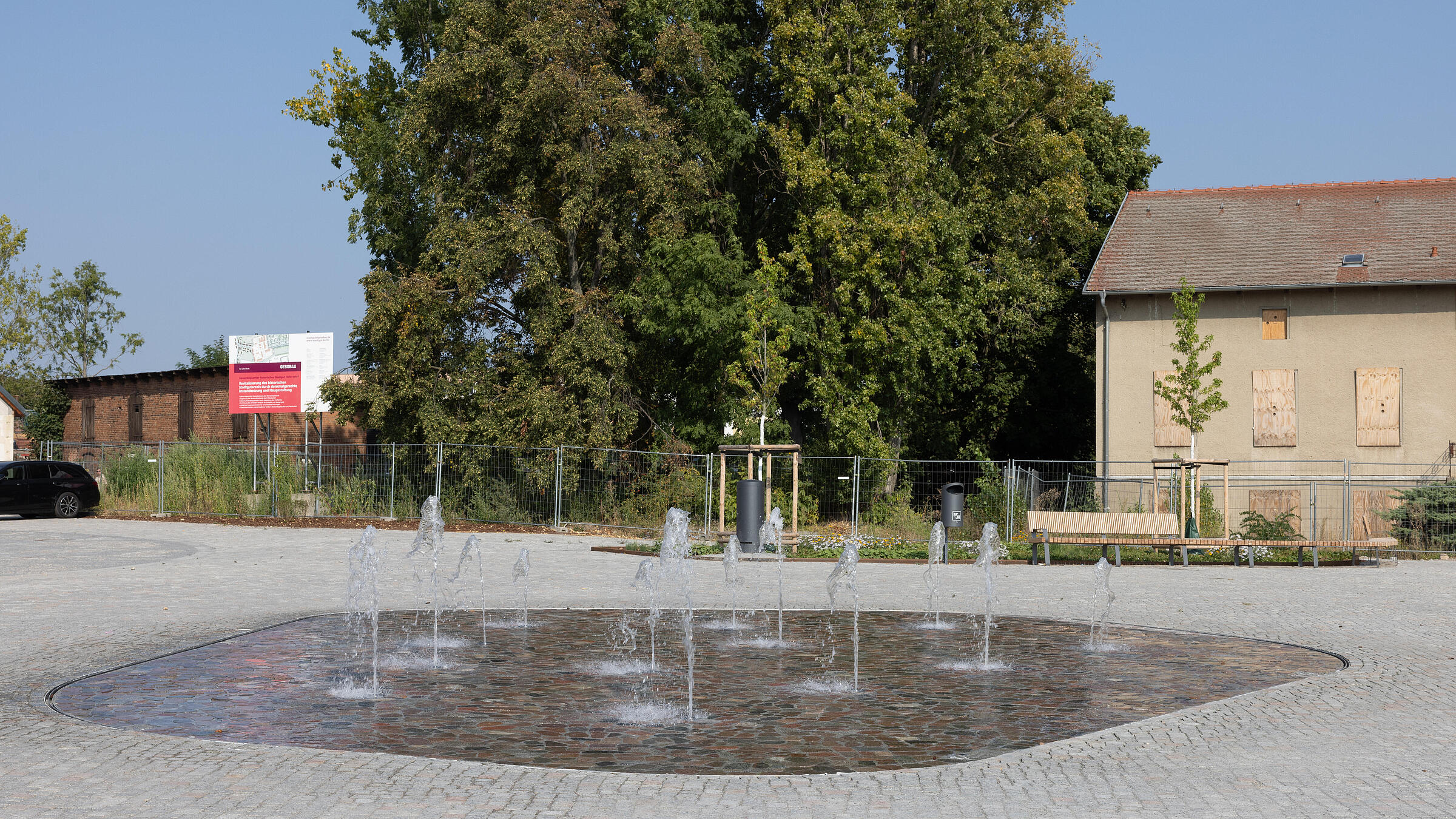 Fot zeigt ein Wasserspiel inmitten eines Platzes aus Pflasterstein.