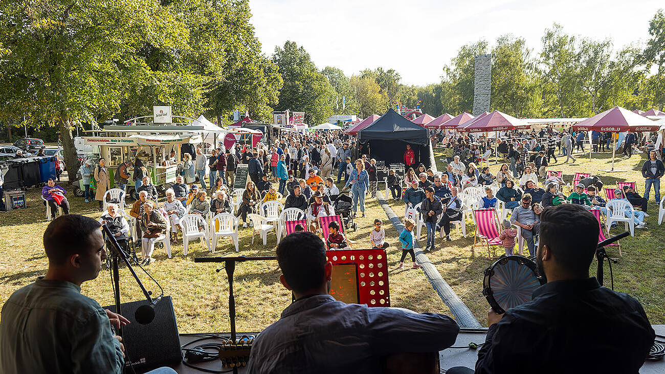 Blick in die Besuchermenge beim Begegnungsfest 2024: Mit dem Rücken zur Betrachterin drei Musiker des Haus am See e.V. beim Spielen von arabischen Klängen.