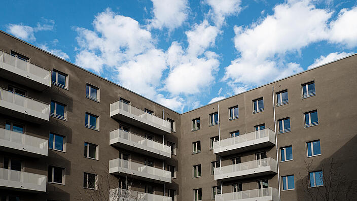 Außenaufnahme zeigt das Wohnhaus Nordbahnstraße vom Innenhof aus gesehen: Eine modern dunkle Fassade mit hellen Balkongittern. 