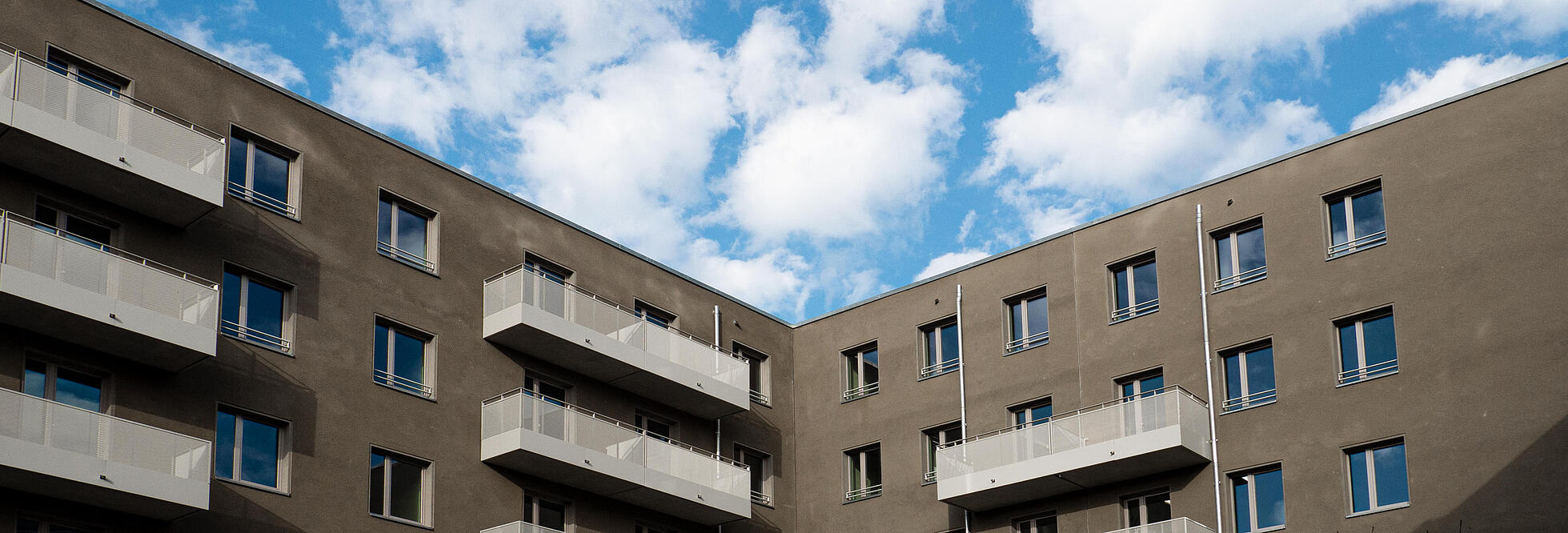 Außenaufnahme zeigt das Wohnhaus Nordbahnstraße vom Innenhof aus gesehen: Eine modern dunkle Fassade mit hellen Balkongittern. 