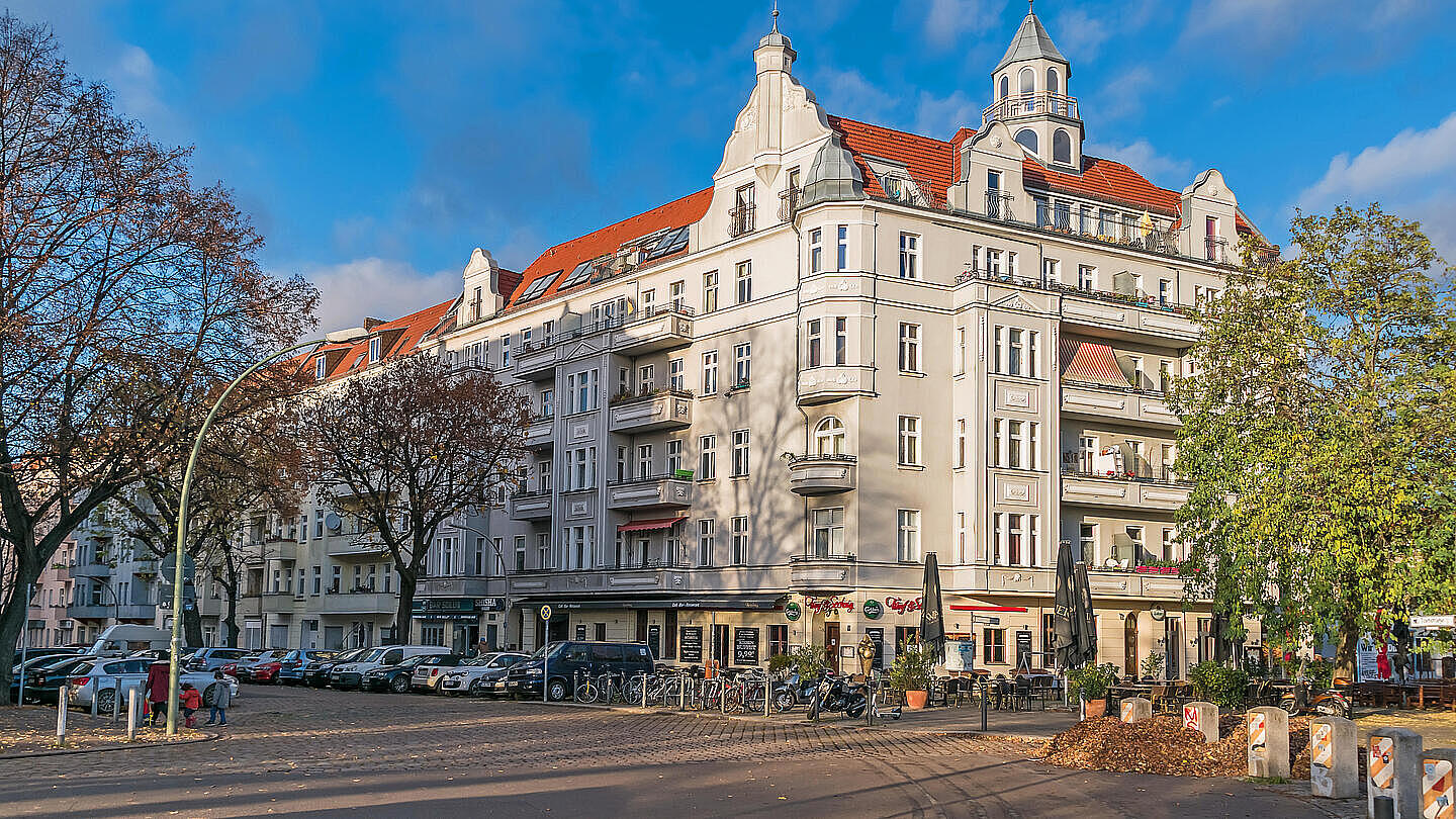 Die herbstliche Außenaufnahme zeigt die Torfstraße im Berliner Bezirk Wedding. Prächtige Altbauten reihen sich am Straßenrand aneinander. Im Erdgeschoss an der Ecke befindet sich ein Restaurant mit Draußenbestuhlung. Am rechten Bildrand befindet sich ein noch grün blühender Baum sowie ein Laubhaufen.