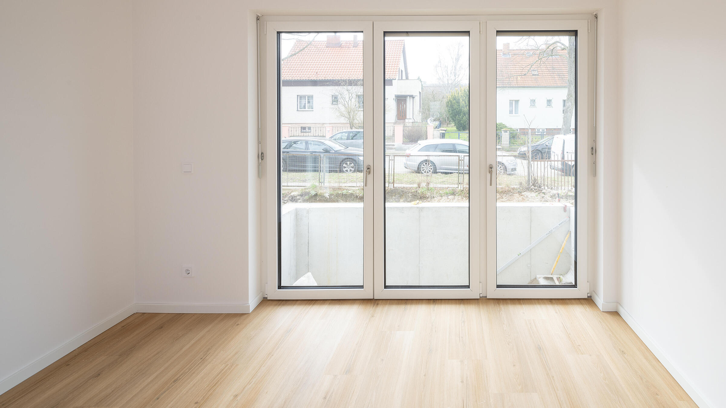 helles, modernes Zimmer mit Boden in Holzoptik und Balkonfenstern