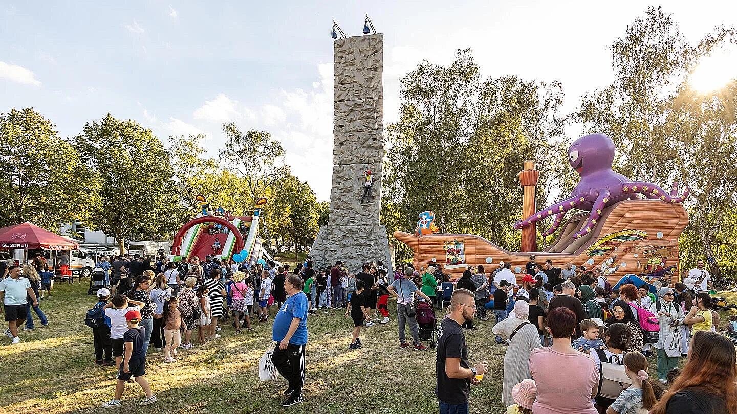 Außenaufnahme zeigt den Kinderspielbereich auf dem Begegnungsfest: ein Kletterturm, eine Hüpfburg in Form eines Piratenschiffs und eine aufblasbare Rutsche.