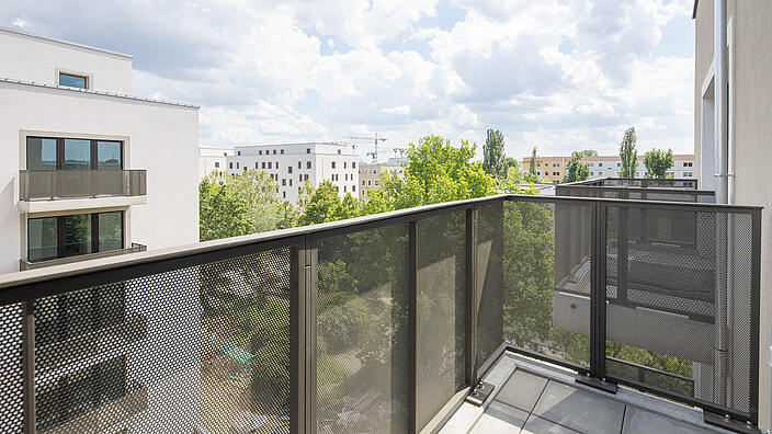 Blick von einem modernen Balkon ins Grüne und mit Sicht auf moderne Wohnhäuser