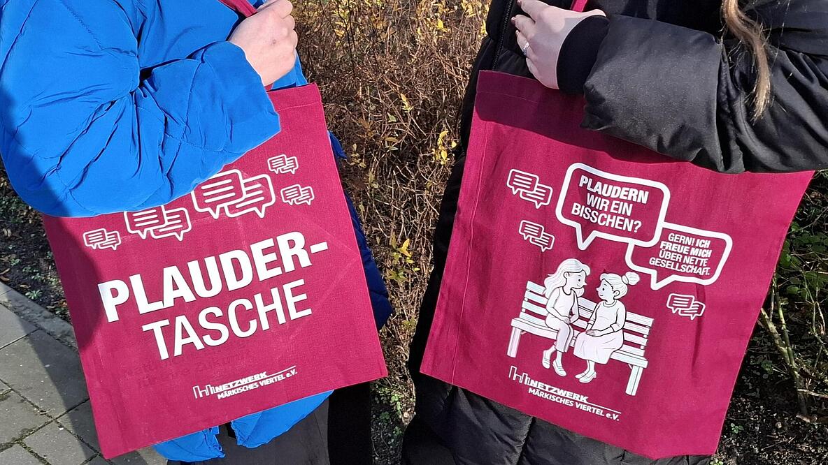 Bild zeigt zwei Personen, sich zugewandt mit jeweils einer Plaudertasche (Jutebeutel mit Print).