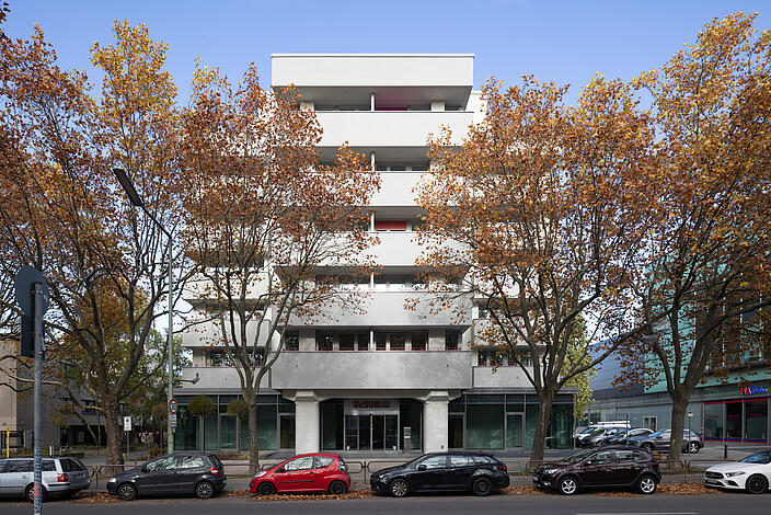 Bild zeigt Frontantsicht des neu gestalteten Wohn- und Geschäftsgebäudes im Wilhelmsruher Damm 142, Außenaufnahme. Im Vordergrund Bäume und parkende Autos.